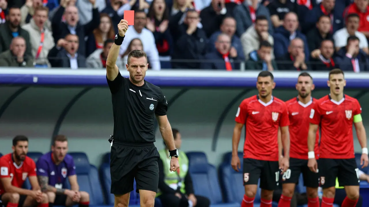 Rozhodčí drží červenou kartu, hráč odchází z hřiště